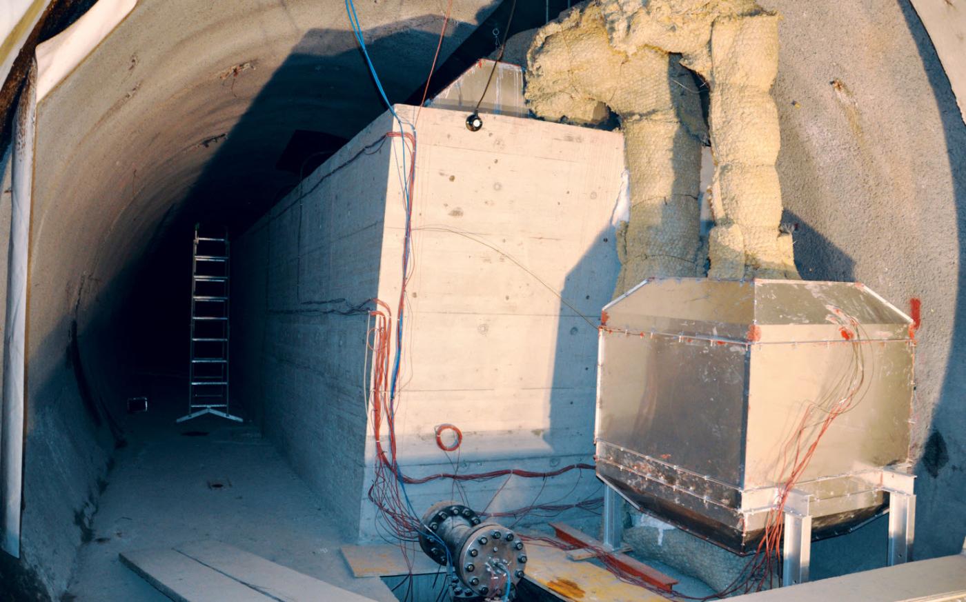 Sensibel-latenter thermischer Speicher in der Pilotanlage bei Pollegio. Links ist der mit Kieselsteinen gefüllte sensible Speicher, rechts der latente Speicher zu sehen. Der sensible Speicher ist 3,1 m hoch, 9,9 m lang und 4 m breit. Der latente Speicher ist etwa 1,5 m hoch, lang und breit.